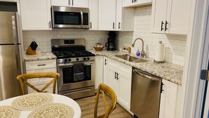 Una cocina moderna con armarios blancos, electrodomésticos de acero inoxidable, encimera de granito y una mesa de comedor de madera con manteles individuales estampados.