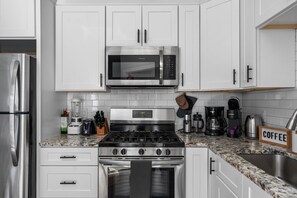 Una cocina moderna con gabinetes blancos, electrodomésticos de acero inoxidable, estufa a gas, microondas y una estación de café.