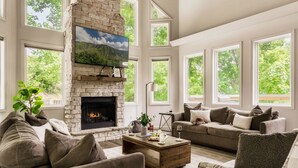A spacious living room with a stone fireplace, large windows, and a comfortable seating area. - Hot Tub/Game Room/Theater/Fire Pit/VIEWS/Luxury! - Ski View Lodge (Gatlinburg)