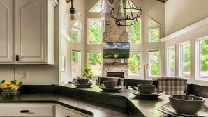 A kitchen with a stone fireplace, large windows, and a dining area with a plaid chair. - Hot Tub/Game Room/Theater/Fire Pit/VIEWS/Luxury! - Ski View Lodge (Gatlinburg)