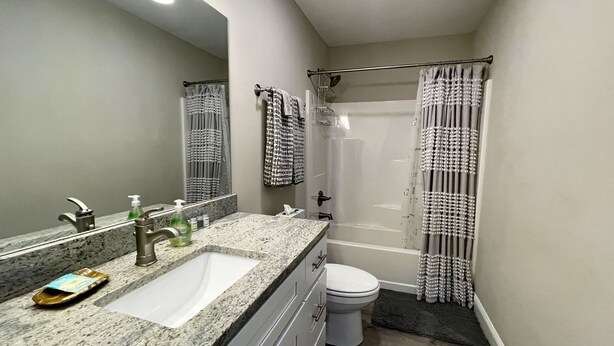 Une salle de bain avec un lavabo sur un plan de travail en granit, un miroir, des toilettes et une douche avec des rideaux à motifs.