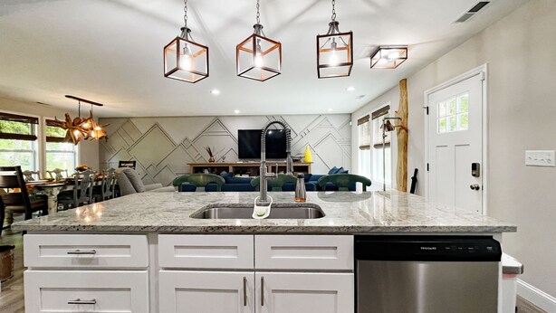 A kitchen with a marble countertop, white cabinets, a stainless steel dishwasher, and a dining area with a table and chairs. - Quiet & Chic 3 BR Cottage w/ Private Garden Near Downtown Asheville (Asheville)