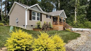 A two-story house with a front porch, a covered deck, and a small front yard with yellow flowering bushes. - Quiet & Chic 3 BR Cottage w/ Private Garden Near Downtown Asheville (Asheville)
