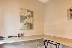 Une pièce avec un sol carrelé, un tableau représentant des fleurs au mur, une petite table avec des stylos et une bouteille, et une prise de courant.