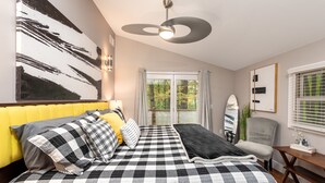 Ein Schlafzimmer mit kariertem Überwurf, gelbem Kopfteil und einem großen abstrakten Gemälde an der Wand.