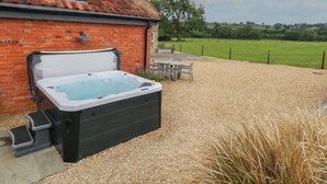 A hot tub next to a brick building with a tiled roof, surrounded by gravel and a grassy field. - Swallows Nest (Sturminster Newton)