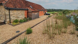 A rustic barn with a sloped red-tiled roof, stone walls, and a gravel driveway. - Swallows Nest (Sturminster Newton)