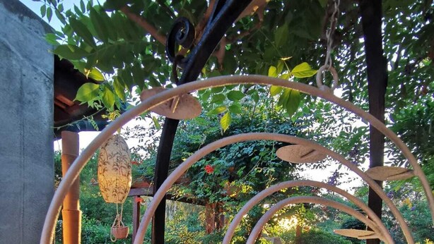 A spiral metal sculpture with a hanging ornament, surrounded by greenery and a paved area with chairs. - La Magnolia Casa Vacanze (Sicilia)