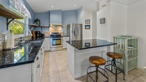 A modern kitchen with a central island, stainless steel appliances, and a bar stool area. - Isle Relax: Close to Gulf of Mexico and Pine Ave. (Anna Maria)