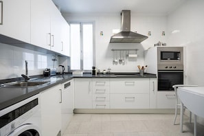 Une cuisine moderne avec des meubles blancs, une hotte en acier inoxydable, un four encastré et un lave-vaisselle.