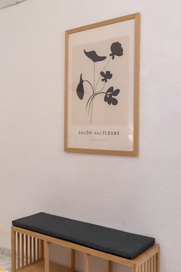 Sur un mur, on peut voir une estampe botanique encadrée intitulée « SALON des FLEURS », et en dessous, un banc en bois.