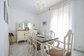 Un comedor con una mesa blanca, sillas y una araña.
