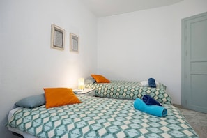 Une chambre avec deux lits, chacun agrémenté de draps et d’oreillers à motifs, une table de chevet avec une lampe et une porte.