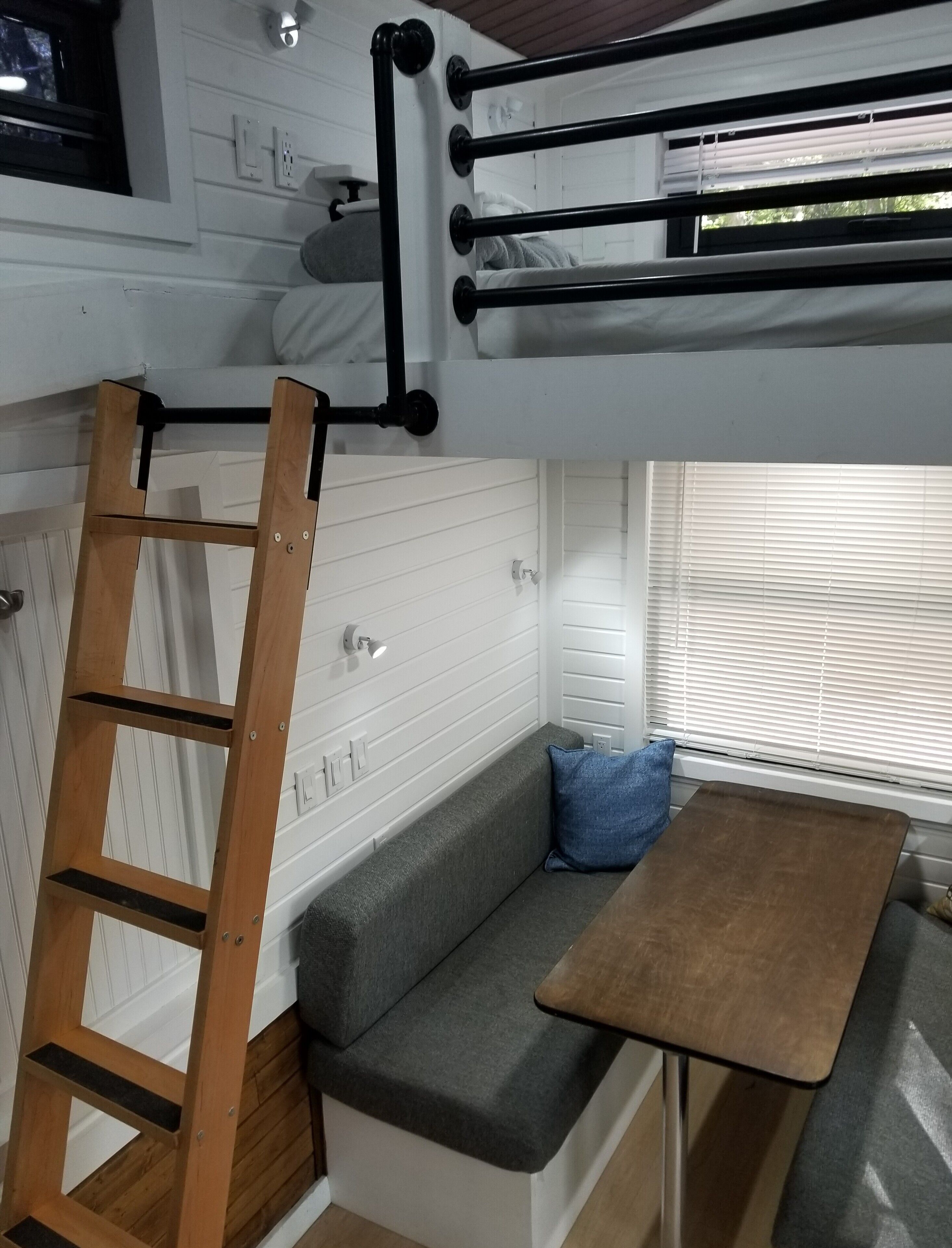 Eine kompakte Küchenzeile mit einer Bank und einem Tisch, einer Holzleiter und einem Etagenbett mit Kopfteil.