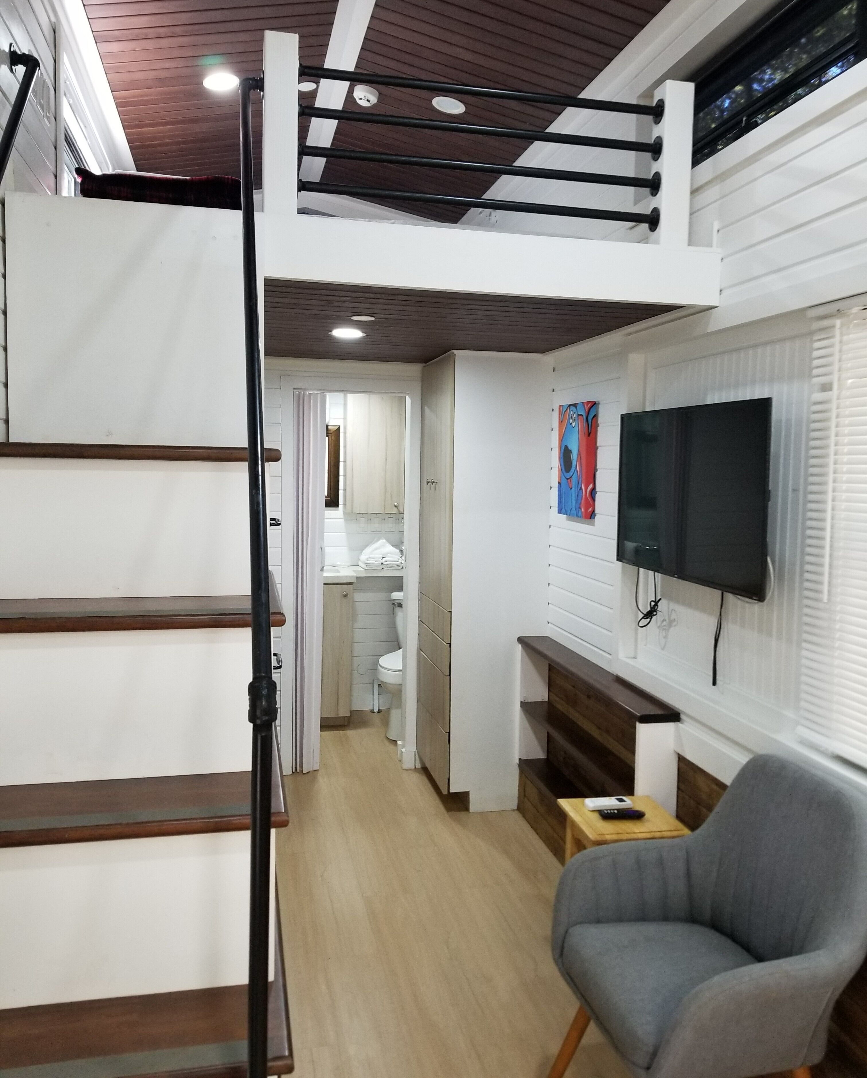 A compact living space with a loft bedroom, a bathroom, and a seating area with a television.