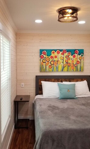 Um quarto com uma cama, uma mesinha de cabeceira, um quadro e um lustre.