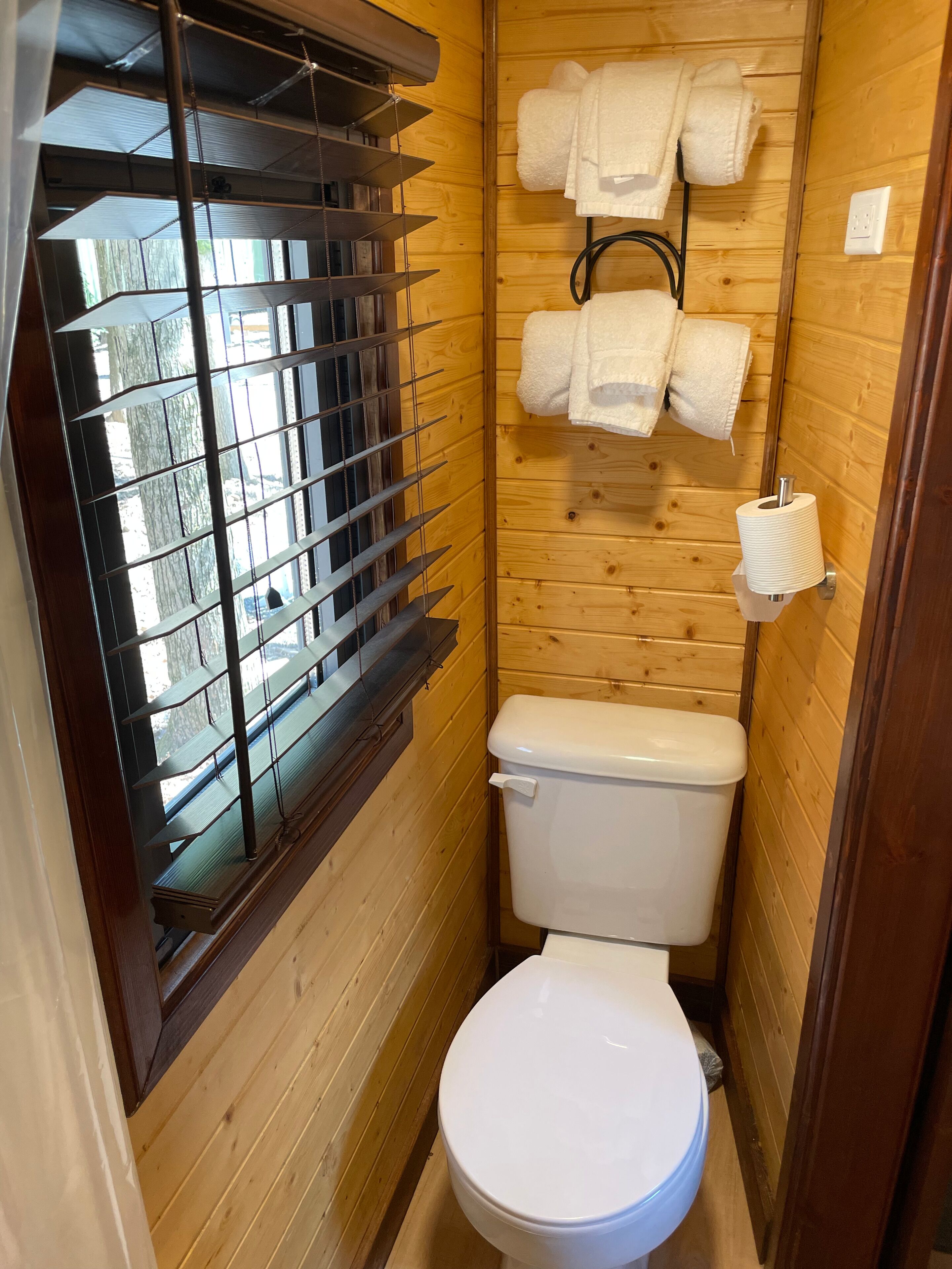 Un baño pequeño y funcional con inodoro, una ventana con persianas y un perchero con toallas.