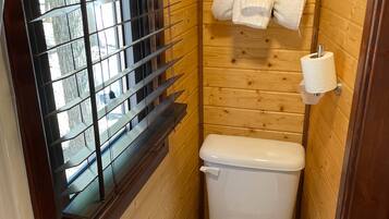 Un baño pequeño y funcional con inodoro, una ventana con persianas y un perchero con toallas.