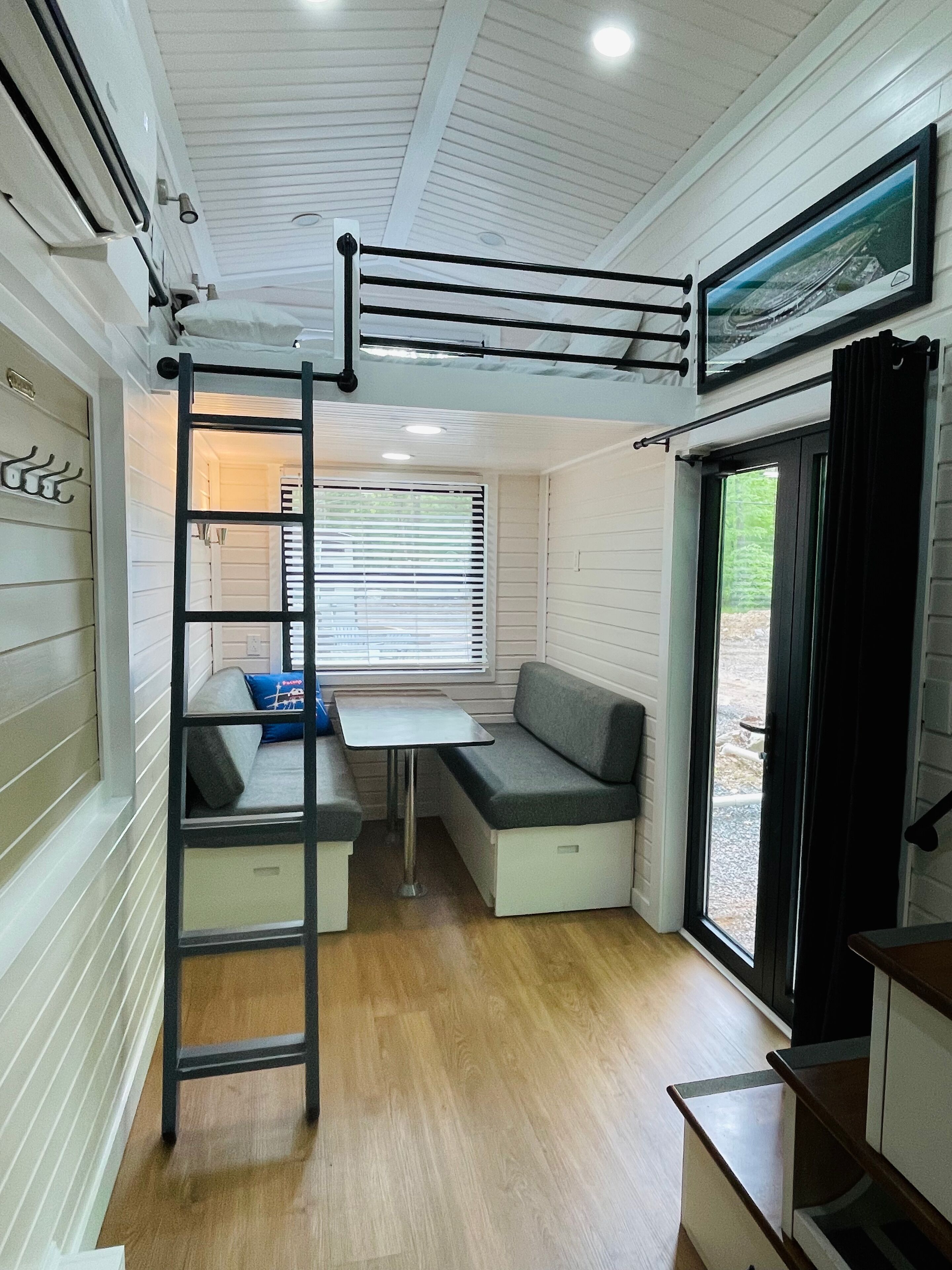 A compact, well-lit room with a loft bed, a small table, and a bench.