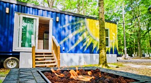 Uma casa móvel azul e amarela com uma lareira à lenha em frente.