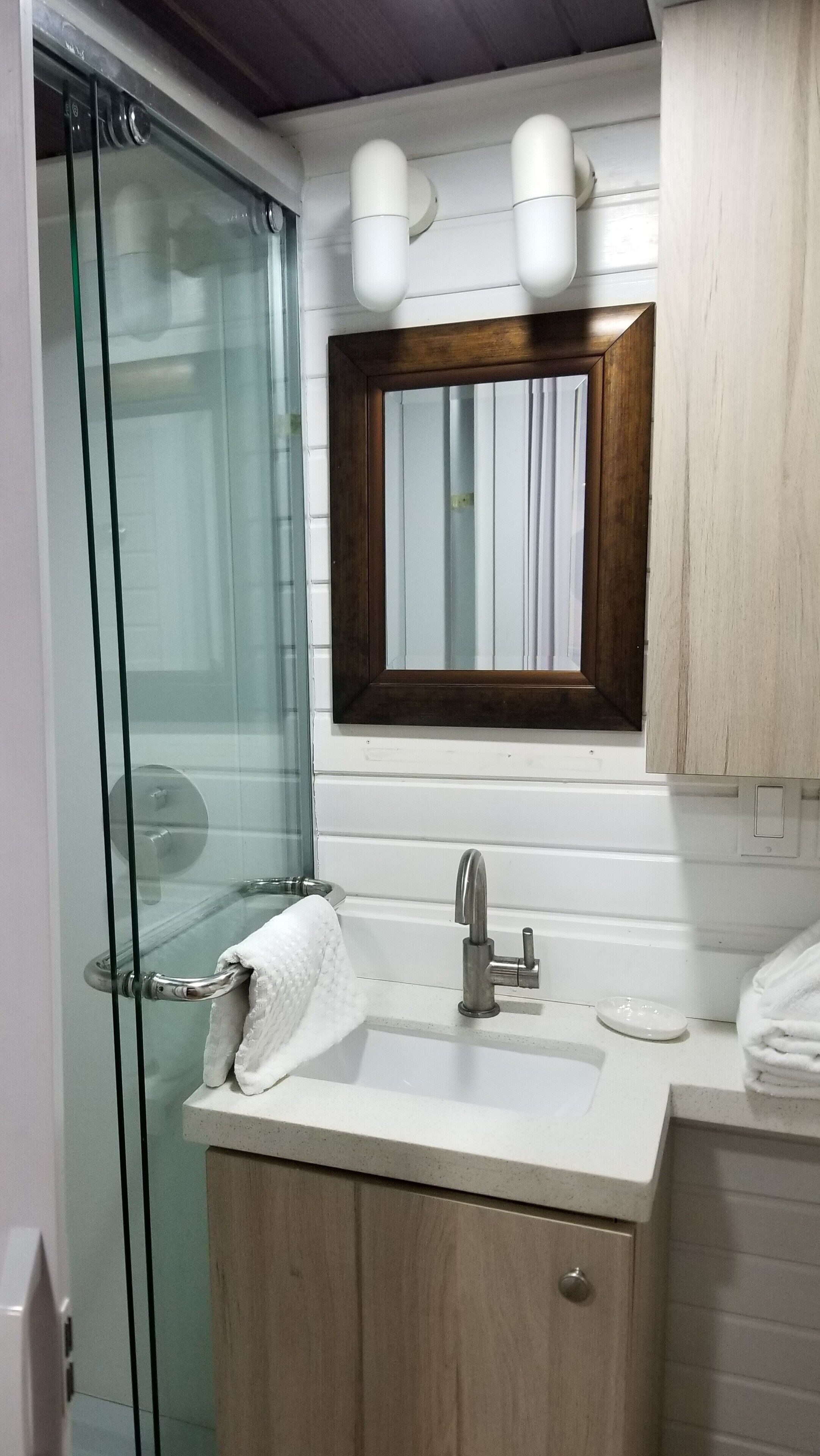 Un bagno con box doccia in vetro, un lavandino con specchio sopra e mobili contenitori in legno.