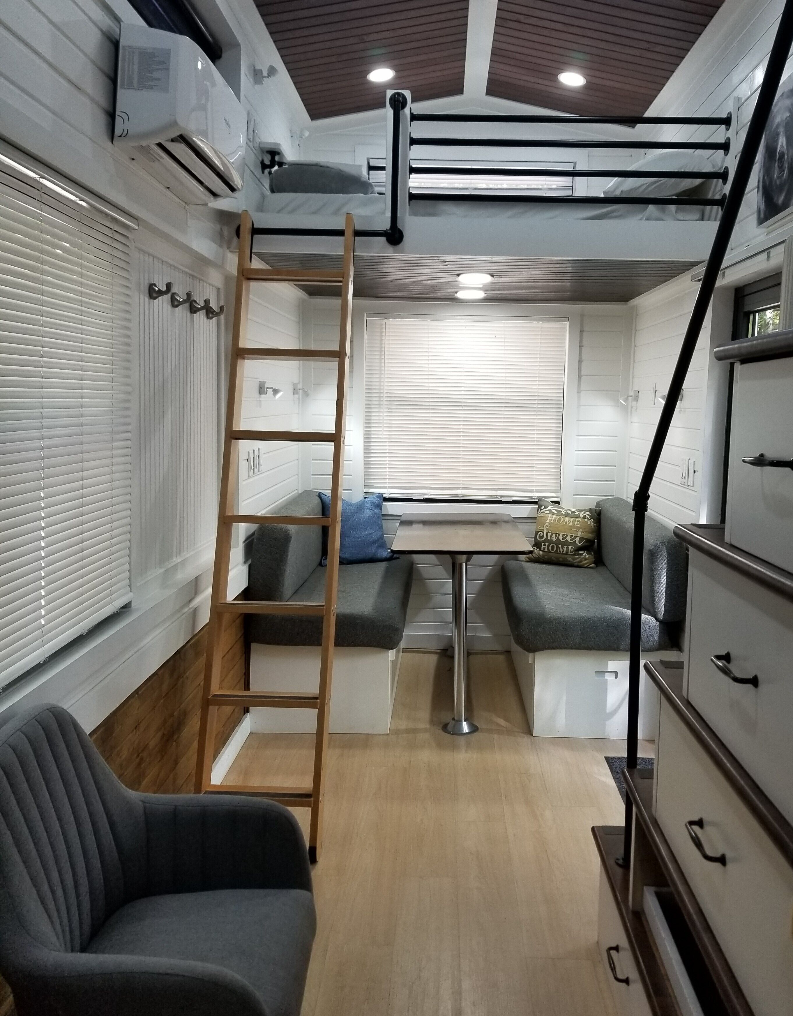 A compact, modern interior with a loft bed, a ladder, a sofa, and a small table.