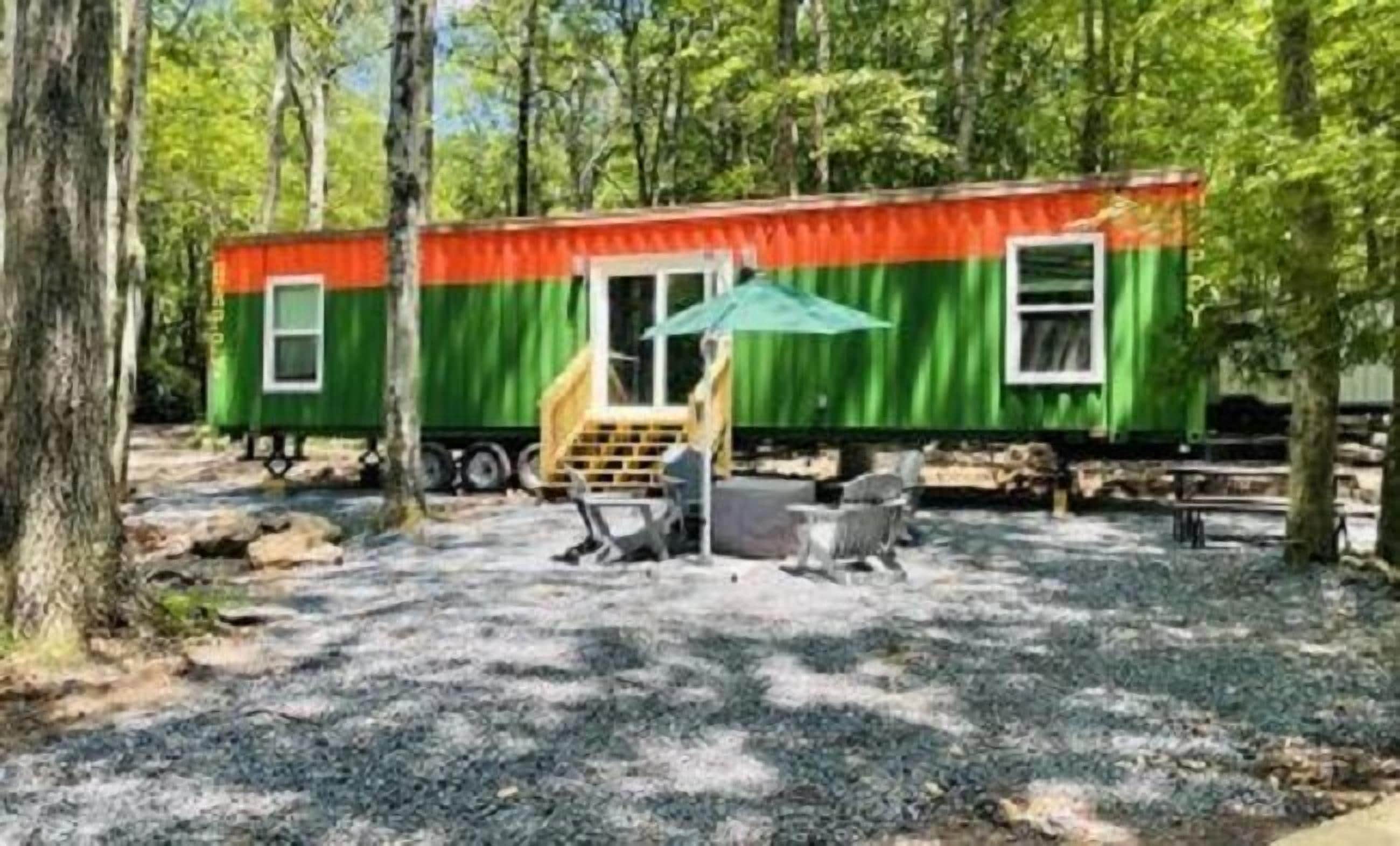 A small, single-story cabin with a green and orange exterior, a porch with a bench, and a table.