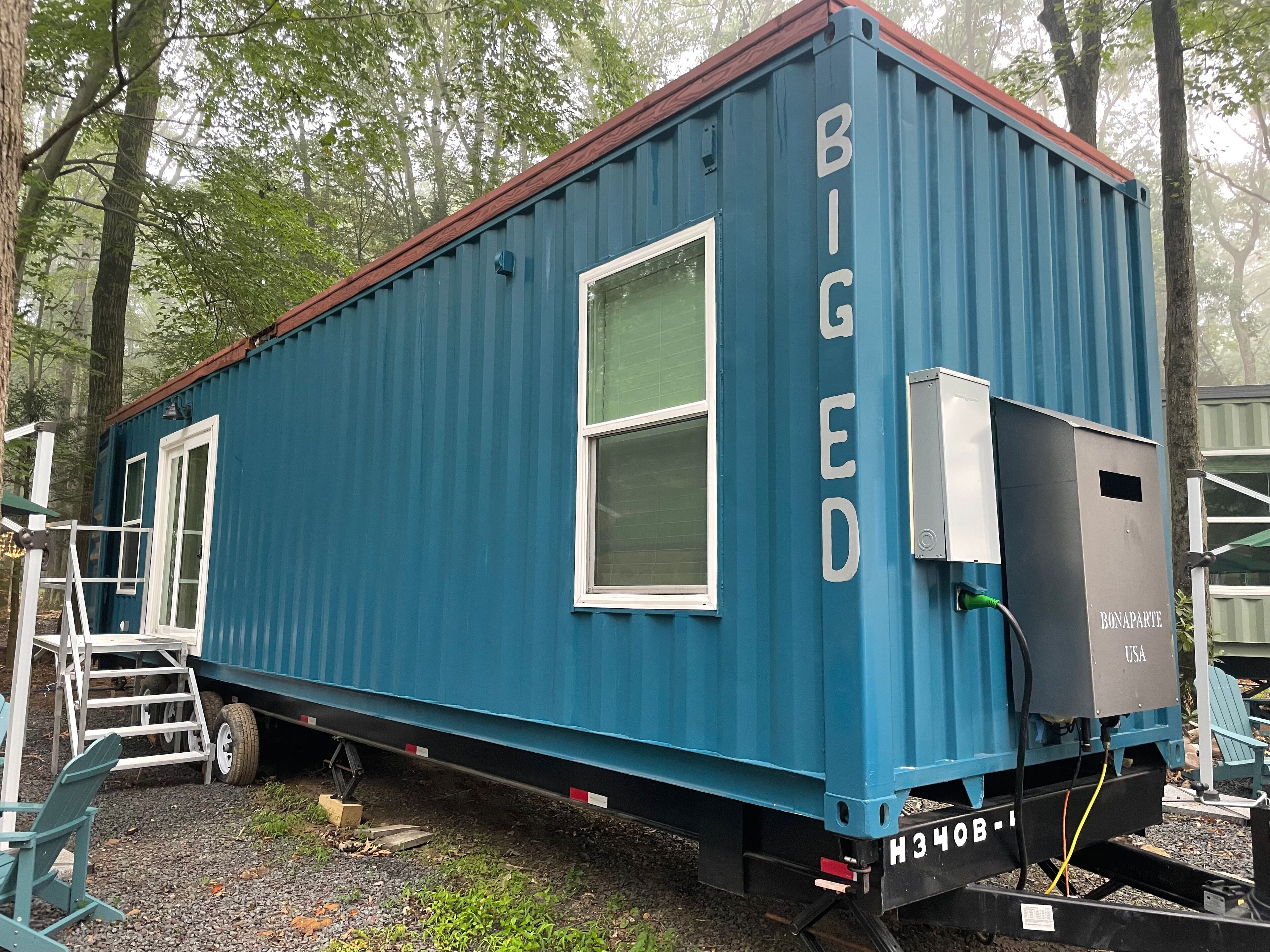 A blue mobile home with the word "BIGGED" on its side, a window, and a power outlet.