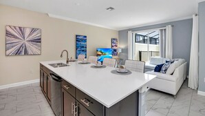 A modern kitchen with a central island, a dining area with a white table and chairs, a sofa, and artwork on the walls. - EV_2861 - 4BR / 3BA Storey Lake Townhome near to Disney, Private Pool & Resort (Kissimmee)