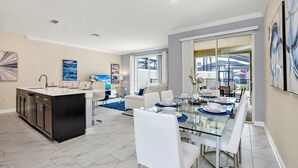 A modern kitchen with a central island, a dining area with a glass table, and a living space with a sofa and coffee table. - EV_2861 - 4BR / 3BA Storey Lake Townhome near to Disney, Private Pool & Resort (Kissimmee)