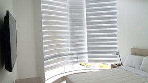 A bedroom with a bed, a TV mounted on the wall, and a window with blinds.