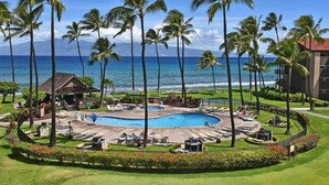 A resort with a central pool, palm trees, and a view of the ocean.
