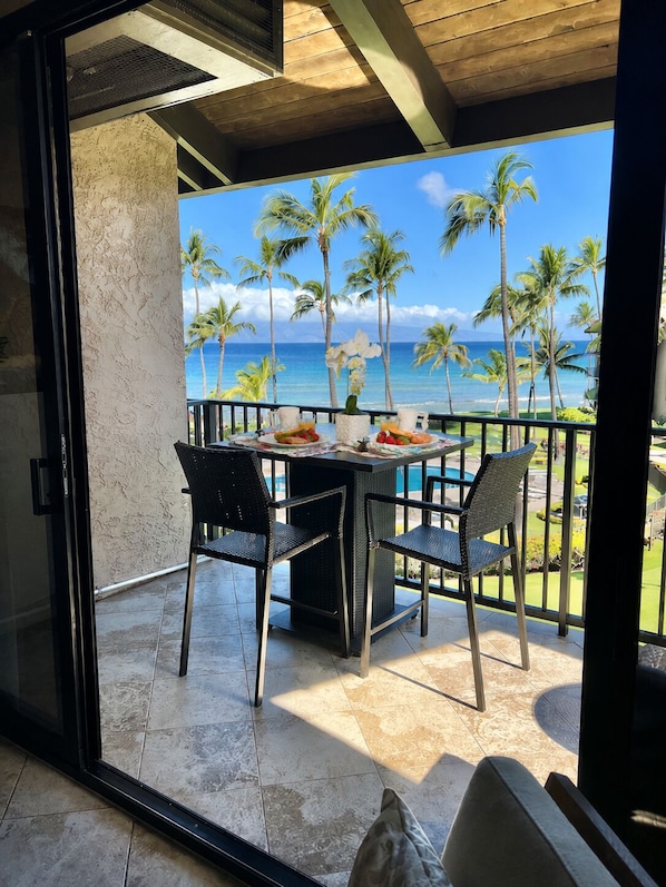 A balcony with a table, chairs, and a view of the ocean and palm trees.