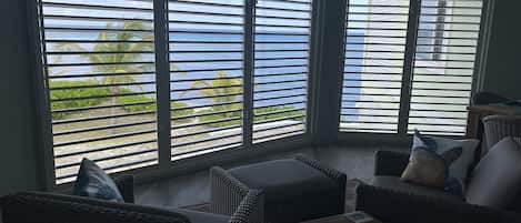 A room with a view of the ocean through large windows, wicker furniture, and a small table with a vase.