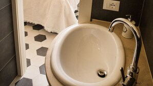A bathroom with a white sink, a shower, and a bed in the background. - Luxury apartment residence "La Fontana" (Lucca)