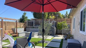 Un jardin avec un patio, du mobilier d’extérieur, une balançoire et un parasol rouge.