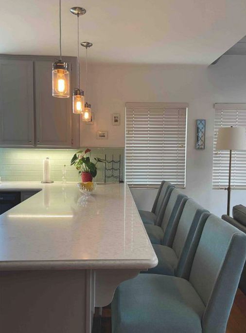 A modern kitchen with a central island, pendant lighting, and a dining area with chairs.