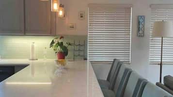 A modern kitchen with a central island, pendant lighting, and a dining area with chairs.