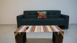 A living room with a dark green sofa, a colorful striped coffee table, and a decorative pillow.