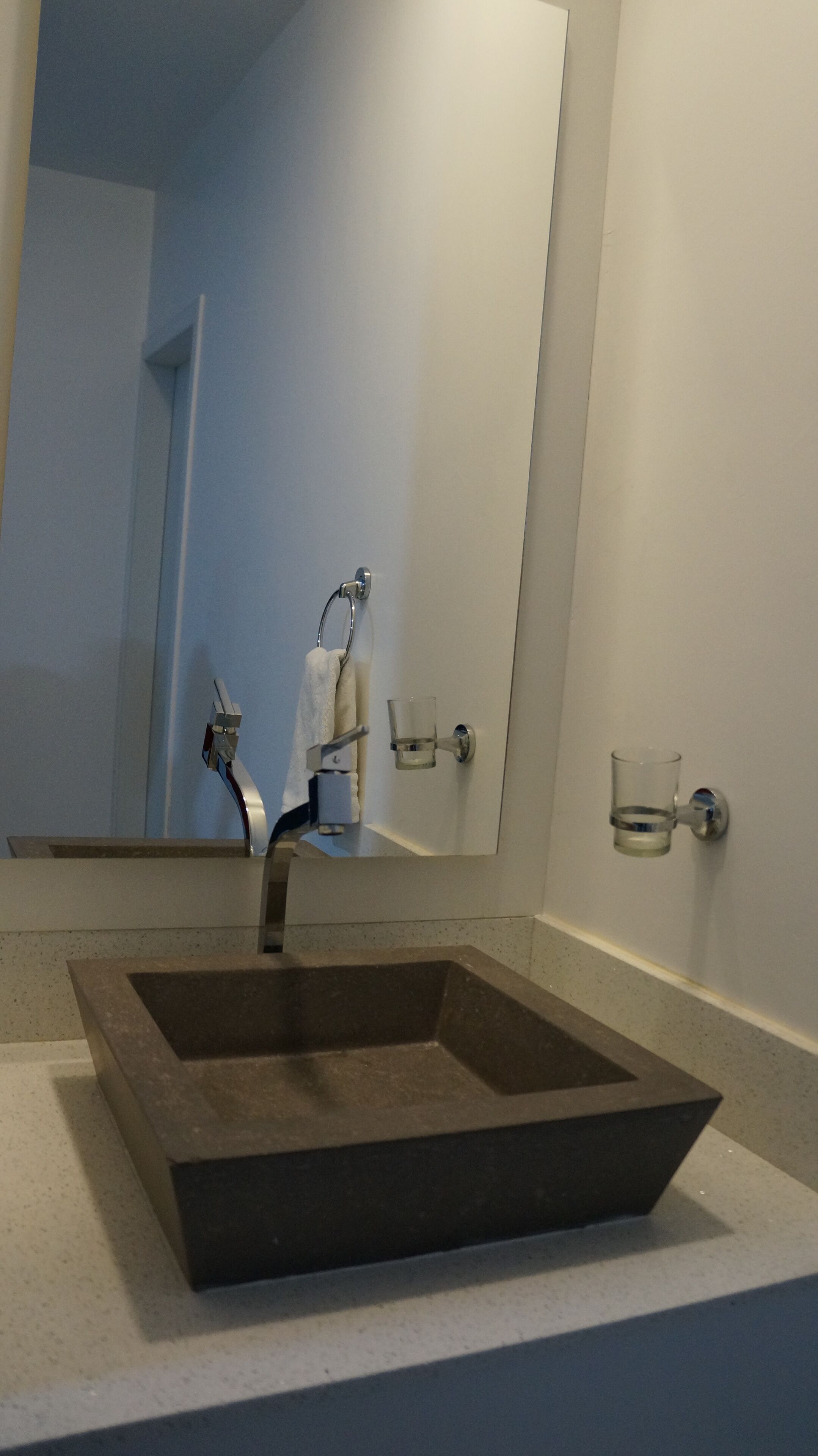A bathroom with a large mirror, a square sink, and two glass cups mounted on the wall.
