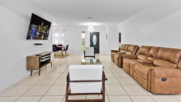 A spacious living room with a large leather sofa, a white armchair, a glass-top coffee table, and a flat-screen TV mounted on the wall. - Private lakefront charming Home in Miami/Pembroke (Pembroke Pines)