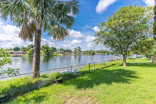 Um parque com um lago, uma palmeira e uma área gramada com cerca.