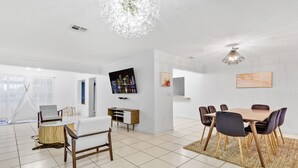 A modern living room with a dining area, a TV mounted on the wall, and a large window with sheer curtains. - Private lakefront charming Home in Miami/Pembroke (Pembroke Pines)