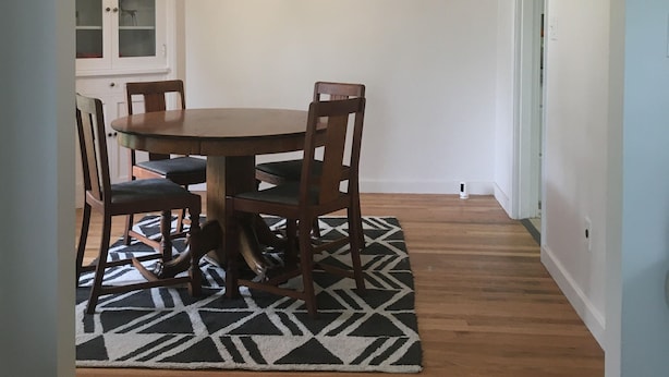 A dining area with a wooden table and chairs, a patterned rug, and wall-mounted artwork. - Oak Street Farm House (Omak)