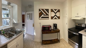A compact kitchen with white cabinets, a stainless steel sink, a microwave, and a stove. There are abstract wall art pieces above the microwave. - Oak Street Farm House (Omak)