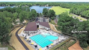 An aerial view of a resort with a large swimming pool, a covered area, and a lake in the background. - Beautiful, spacious, lakefront home large lot, firepit, hot tub, and more  (Locust Grove)