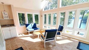 A bright room with large windows, a ceiling fan, and a kitchen area with white cabinets. - Beautiful, spacious, lakefront home large lot, firepit, hot tub, and more  (Locust Grove)