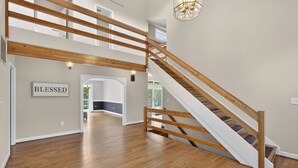 A spacious interior with a wooden staircase, a sign reading 'BLESSED,' and a view of the outdoors. - Beautiful, spacious, lakefront home large lot, firepit, hot tub, and more  (Locust Grove)