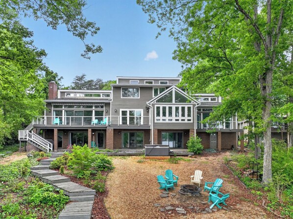 A modern two-story house with a covered patio, outdoor seating, and a wooden deck leading to the entrance.