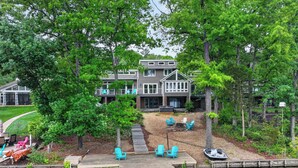 A lakeside lodge with a dock, outdoor seating, and a well-maintained lawn. - Beautiful, spacious, lakefront home large lot, firepit, hot tub, and more  (Locust Grove)
